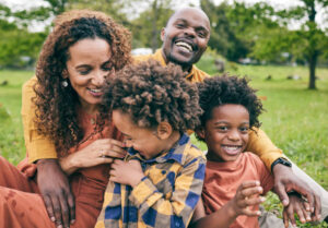 Happy family, parents and children in a park in summer, smile and relax on grass field for quality time, love and nature. Happiness, picnic and portrait of people outdoor and playing together By Goodremedies